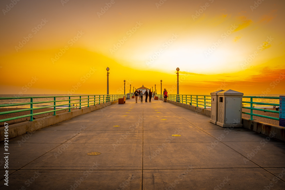 Manhattan Beach Pier at sunset in California. People take pictures, stroll, enjoy the beach. Famous American west coast location for tourists and locals.