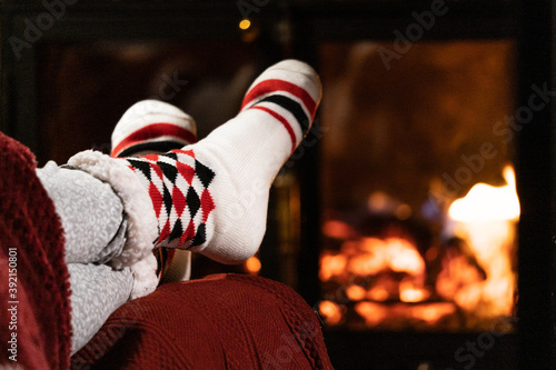 Winter night, happy woman resting by the fire with her feet in wool socks. Cozy scene.