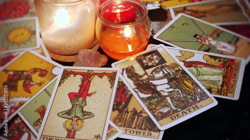 A mystical tarot deck of cards is displayed in a rotation. The hangman and death card are prominent. Candles and crystals are seen in the center of the table.