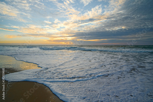 Golden sunset on the beach and low sea waves brake the shore. Tranquil scene, beautiful cloudy sky on background