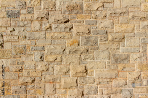 Full frame abstract background of an attractive tan brown natural limestone block wall in ashlar pattern, with rugged texture stone blocks in full sunlight with copy space photo