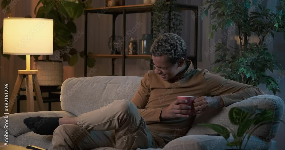 Man having fun watching tv and drinking coffee sitting on sofa at night Man having fun watching tv and drinking coffee sitting on sofa at night