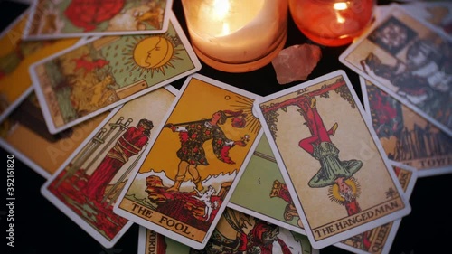 A close up of mystical tarot deck of cards is displayed in a rotation. The fool and hanged man card are prominent. Candles and crystals are seen in the center of the table. photo