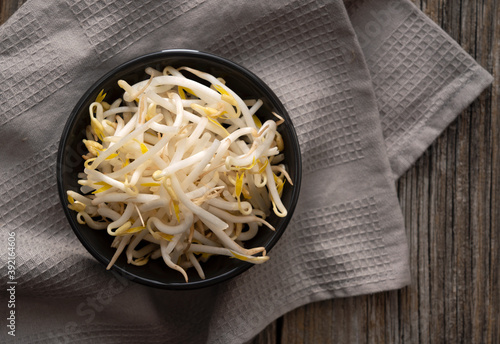 Bean sprouts and cloth in a black bowl set against an old wooden background