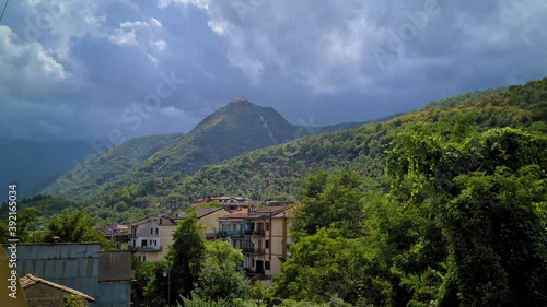 Town hidden in mountain woods, contrasting day light and clouds, Montello, Italy