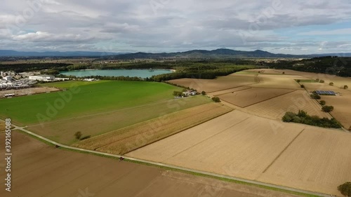 Drone flight backwards from a quarry pond and gravel plant over fields on a cloudy summer day, mountains in the background photo