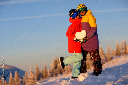 A young couple with a snowy heart in their hands against the background of a winter landscape in the ski resort.