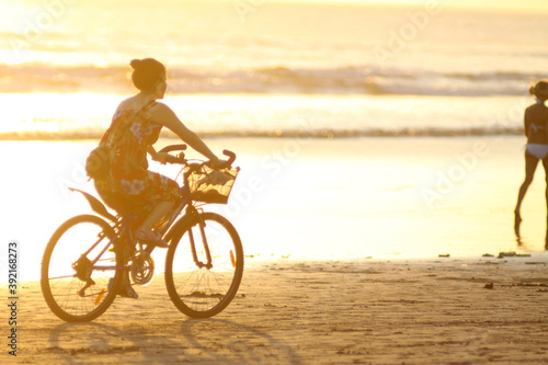 Girl ride bike on the beach at sunset time