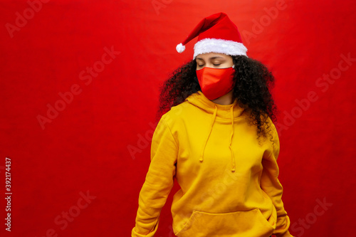 Afro-haired woman with Christmas hat and protective mask against respiratory diseases, covid-19, coronavirus. Red background.