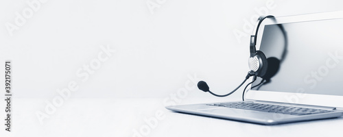 Laptop. Mockup screen and headphones on grey desk and plain background wide banner. Distant learning or working from home, online courses or support minimal concept. Helpdesk or call center headset