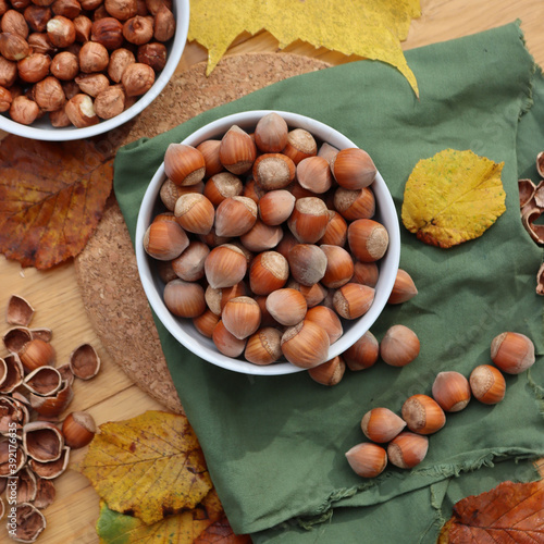 Whole hazenuts in a bowl with cracked hazenuts and autumnal leaves on wooden background photo