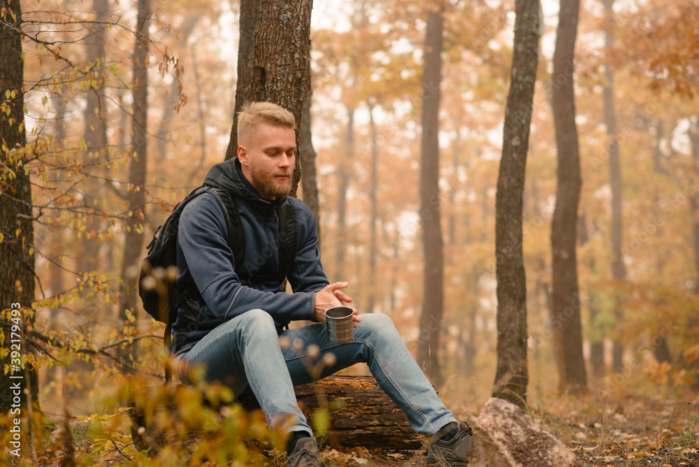 A man traveler in the autumn forest rests on a halt and drinks tea. A man traveler in the autumn forest rests on a halt and drinks tea.