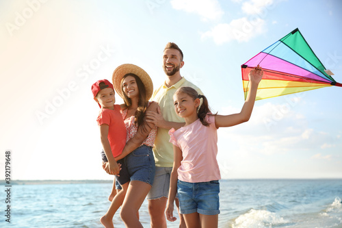 Happy parents and their children playing with kite near sea. Spending time in nature