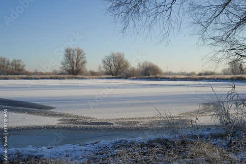 Breath of winter, first ice on the lake, dawn on a frosty morning with frost on the grass, close-up of frost, patterns on the first ice.