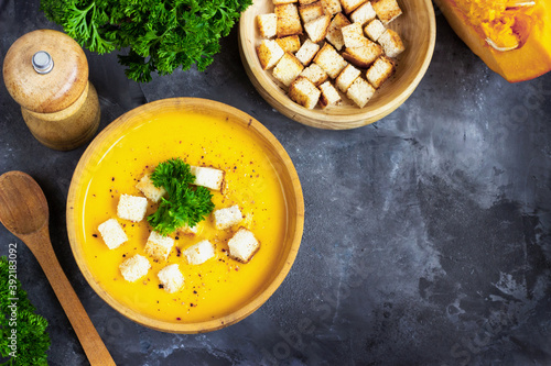 Pumpkin soup with cream, bread and fresh parsley in a rustic metal plate over grunge black background. Top view, copy space
