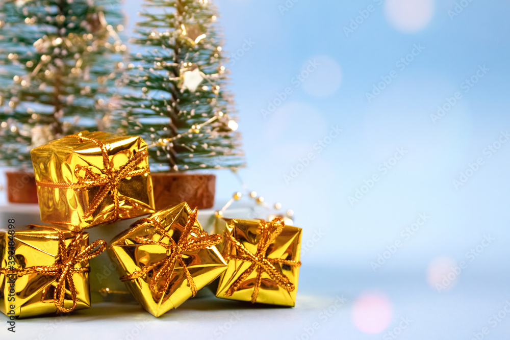 Closeup view of trendy Christmas and New Year composition with Christmas tree, present boxes, decorations and bokeh lights on pastel blue background with copyspace. Selective focus