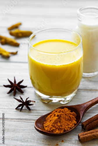 Yellow turmeric latte drink. Golden milk with cinnamon, turmeric, ginger and honey over white wooden background.