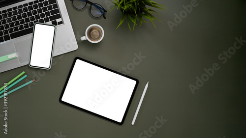 Top view of Contemporary workspace with isolated white display tablet, mobile phone, laptop and equipment on gray table.