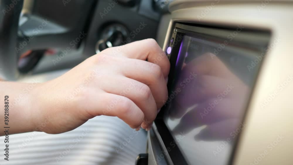Young woman hand with elegant manicure of purple colour rotates grey button at coloured dashboard display in new automobile close view Young woman hand with elegant manicure of purple colour rotates grey button at coloured dashboard display in new automobile close view