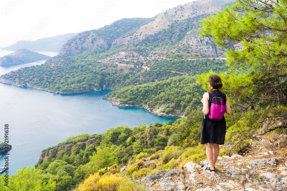 A girl on a trekking trip in the mountains, admires the beautiful natural view of the bay of the sea and the mountains of the mediterranean