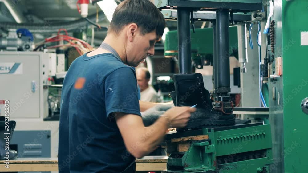Male worker is putting an unfinished boot under a press Male worker is putting an unfinished boot under a press
