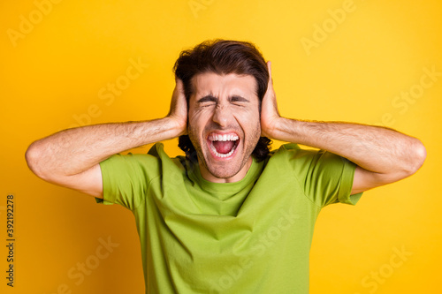 Photo of annoyed mad man palms cover ears open mouth closed eyes wear green t-shirt isolated yellow color background photo