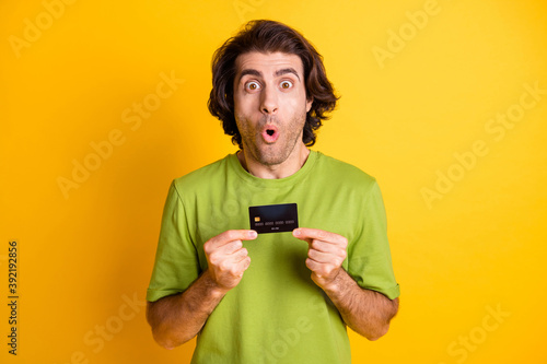 Portrait photo of shocked man demonstrating plastic debit card staring isolated on vivid yellow color background