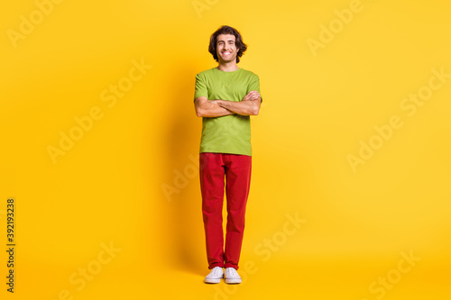 Full length body size photo of smiling confident man with crossed hands wearing colorful clothes isolated vibrant yellow color background © deagreez