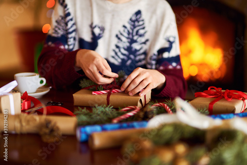  Men's hands hold Christmas present. Man using red ribbon, green fir tree twig to create Christmas gift. Wintar holiday. 