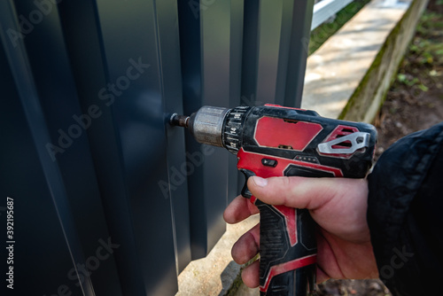 Metal fence installation. The worker is screwing the screw into the metal fence.
