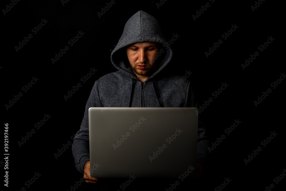 Man in a hood holds a laptop in his hands on a dark background. Concept of cyber rogue, hacker. Banner Man in a hood holds a laptop in his hands on a dark background. Concept of cyber rogue, hacker. Banner