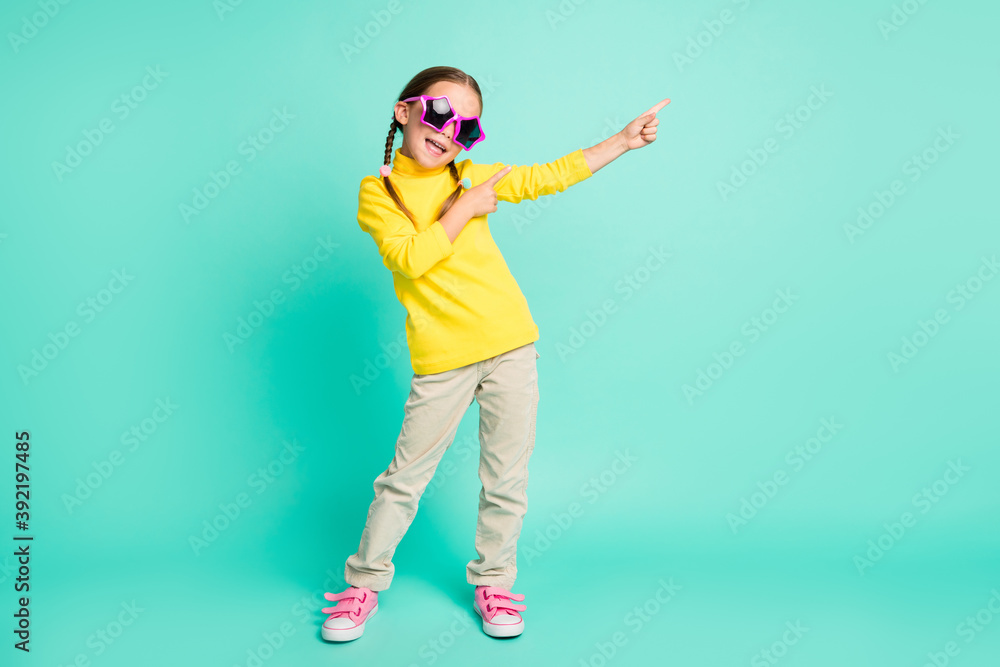 Full length photo of cheerful brown haired girl point empty space wear white pants yellow turtleneck isolated on teal color background Full length photo of cheerful brown haired girl point empty space wear white pants yellow turtleneck isolated on teal color background