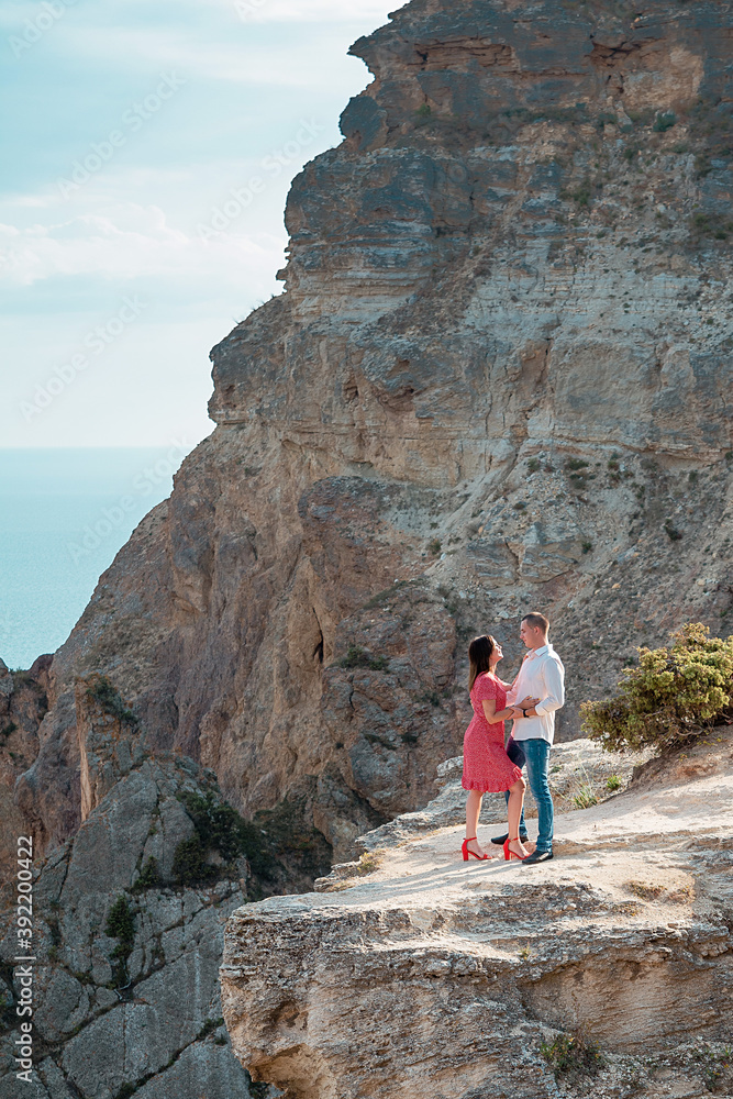Young married couple admires the sea or ocean at edge of a rocky cliff. Family photoshoot on background of crag