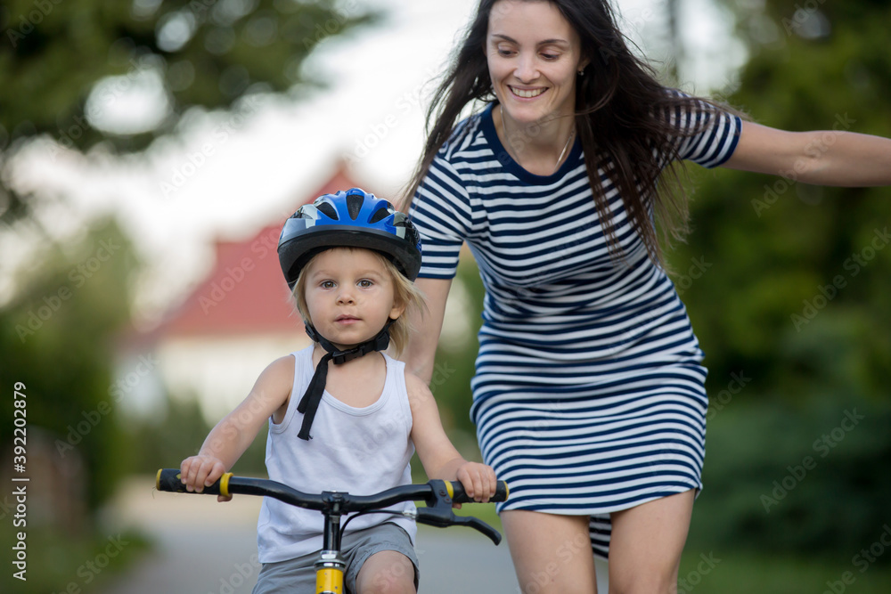 Obraz premium Young mother, helping her son to learn how to ride a bike, holding him and teaching him