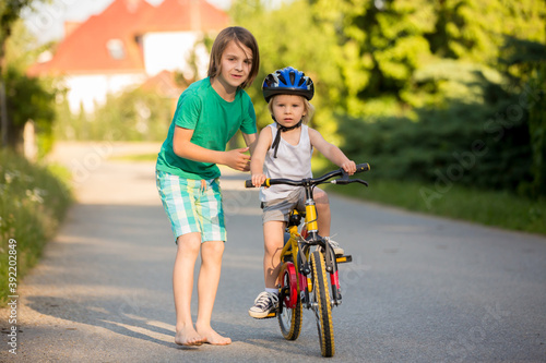 Young mother, helpOlder brother, helping his little brother to learn how to ride a bike, holding him and teaching him bikinging her son to learn how to ride a bike, holding him and teaching him
