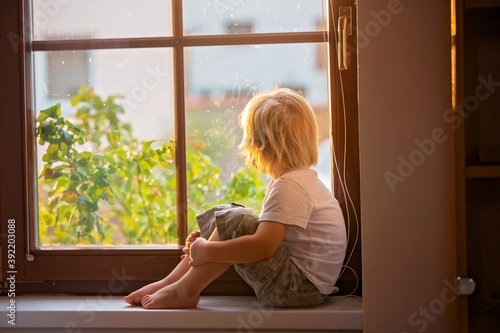 Abandoned little toddler boy, sitting sad on a window shield, looking outside at sunset