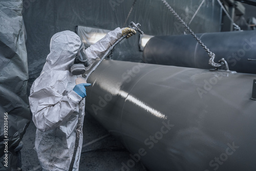 Fototapeta Naklejka Na Ścianę i Meble -  worker wearing protective gear and mask spray painting tanks
