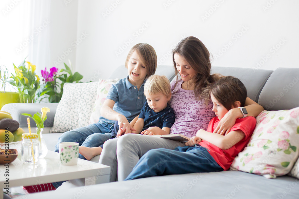 Young woman, mother with three kids, reading a book at home, hugging and laughing Young woman, mother with three kids, reading a book at home, hugging and laughing