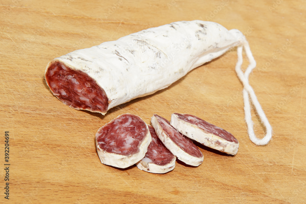 Close-up Italian and Catalonia Fuet cured pork sausage with slices on wooden table. Sausage from minced pork seasoned with pepper - traditional meat product of Western Europe. Selective focus Close-up Italian and Catalonia Fuet cured pork sausage with slices on wooden table. Sausage from minced pork seasoned with pepper - traditional meat product of Western Europe. Selective focus