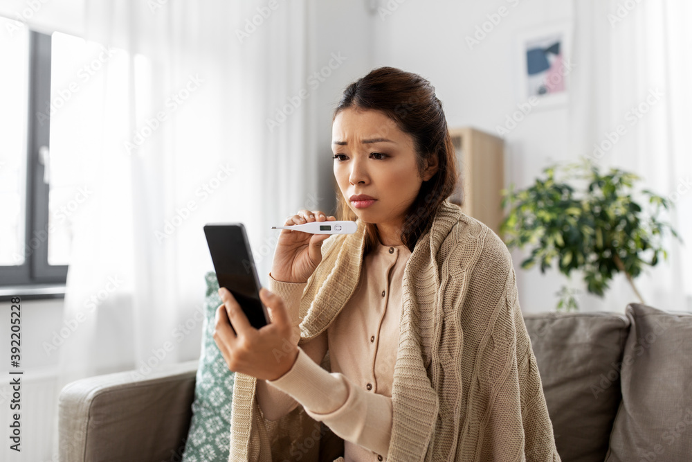 healthcare, technology and people concept - sick asian woman in blanket with thermometer having video call on smartphone at home healthcare, technology and people concept - sick asian woman in blanket with thermometer having video call on smartphone at home