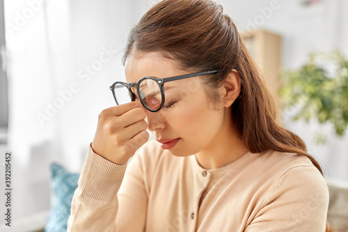 fatigue, stress, vision and people concept - tired asian woman with glasses rubbing nose bridge at home