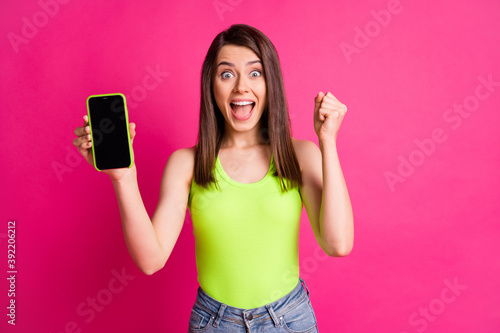 Portrait of young happy girl smile hold smartphone celebrate win victory sale discount raise fist isolated over pink color background