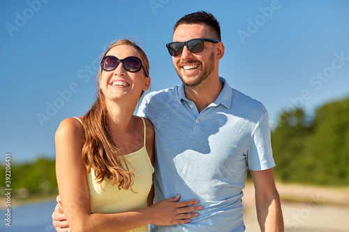 leisure, relationships and people concept - happy couple in sunglasses hugging on summer beach