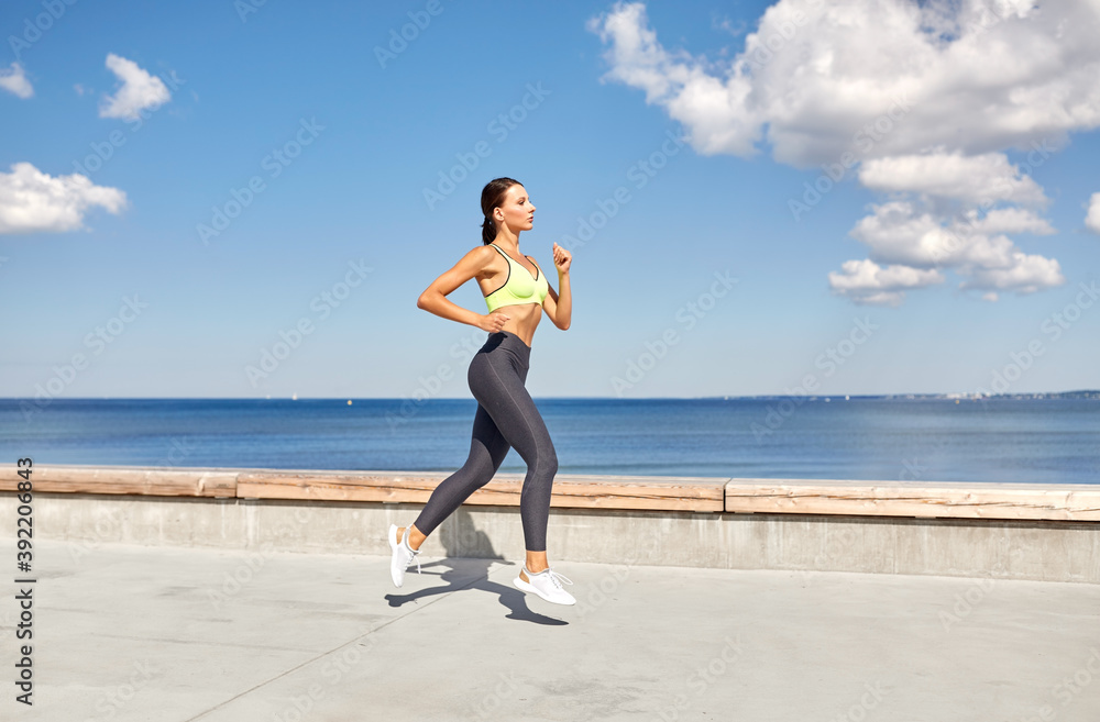 fitness, sport and healthy lifestyle concept - young woman running along sea promenade