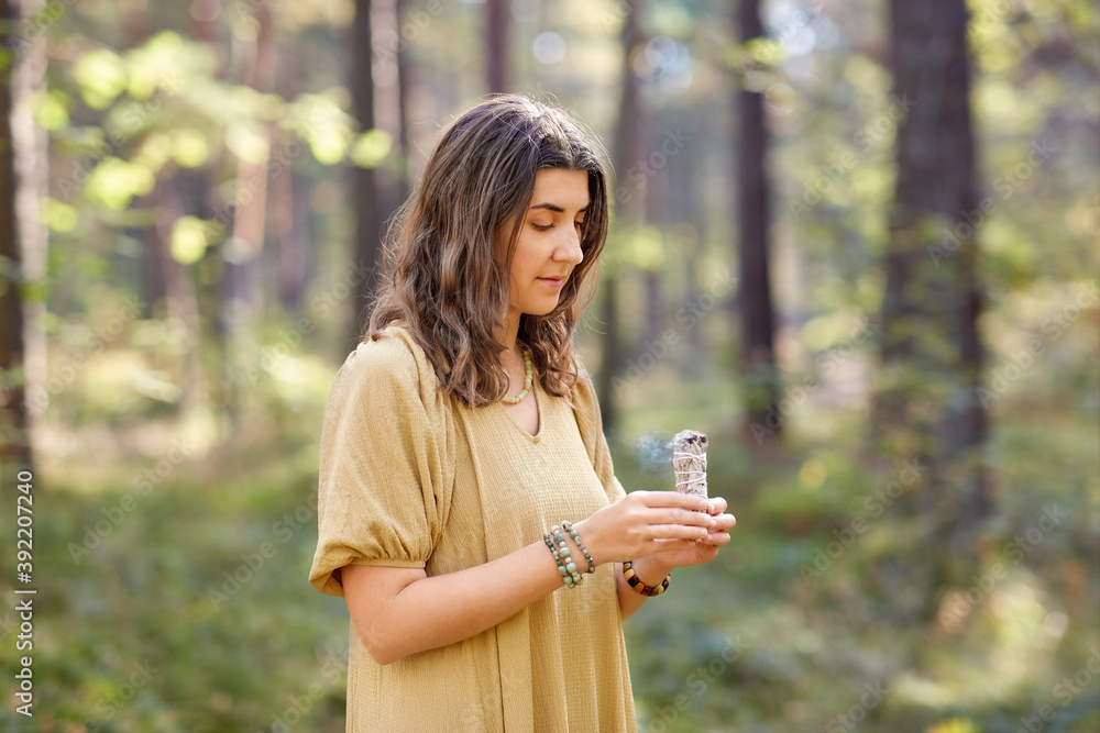 occult science and supernatural concept - young woman or witch with smoking white sage performing magic ritual in forest occult science and supernatural concept - young woman or witch with smoking white sage performing magic ritual in forest