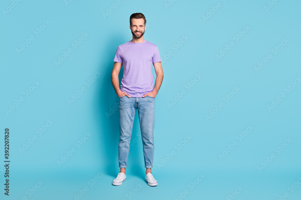 Full size photo of young handsome happy smile man hands in pocket isolated over blue color background Full size photo of young handsome happy smile man hands in pocket isolated over blue color background