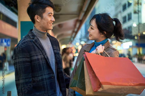 young asian couple standing on street waiting for bus after shopping in the city