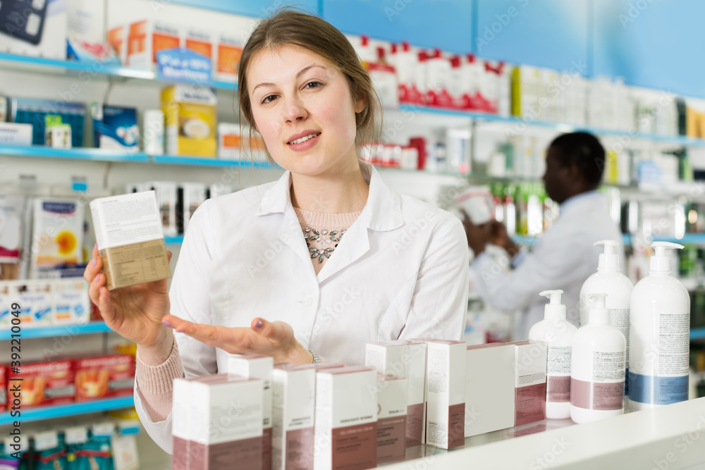 Portrait of attractive young woman pharmacist offering medication in modern pharmacy.