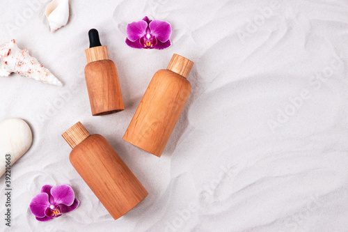 Wooden and glass bottles containers blank mockup for skincare cosmetic products on white sand background with seashells, orchis flowers and stones.