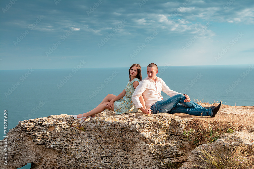 Young married couple admires the sea or ocean at edge of a rocky cliff. Family photoshoot on background of crag